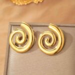 Photo de boucles d'oreilles en spirale dorée, fabriquées en acier inoxydable, posées sur un fond texturé naturel en pierre claire.