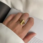 Photo d'une bague dorée ajustable avec un motif de feuille de ginkgo, fabriquée en acier inoxydable, sur fond blanc.