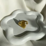 Photo d'une bague dorée ajustable avec un motif de feuille de ginkgo, fabriquée en acier inoxydable, sur fond blanc.