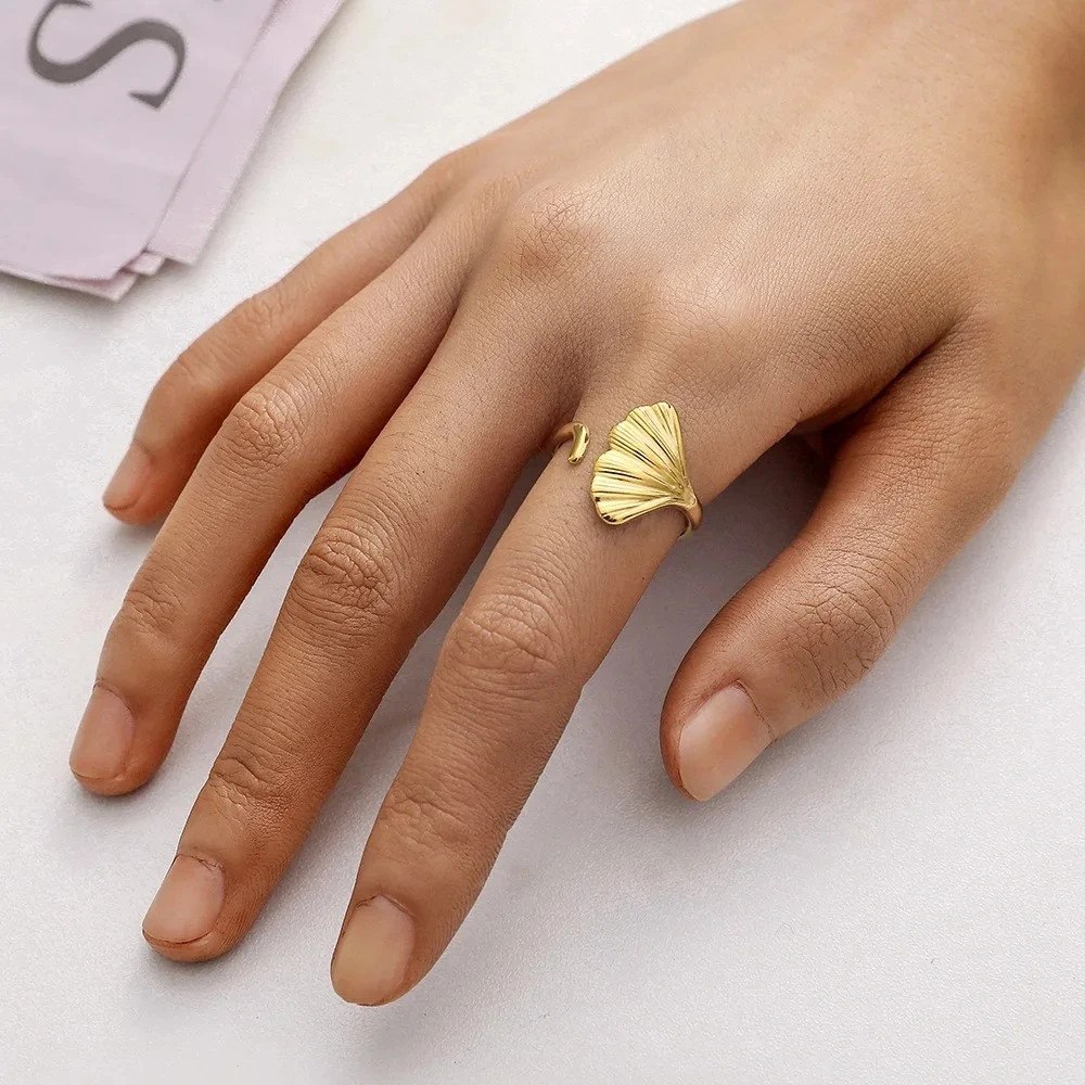 Photo d'une bague dorée ajustable avec un motif de feuille de ginkgo, fabriquée en acier inoxydable, sur fond blanc.