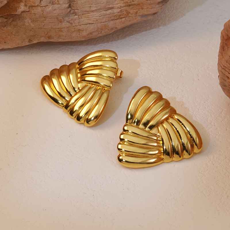 Photo de boucles d'oreilles en éventail doré avec une texture tressée, fabriquées en acier inoxydable, posées sur un fond naturel avec des éléments en bois ou pierre.