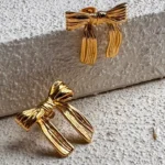 Photo de boucles d'oreilles dorées en forme de nœud, fabriquées en acier inoxydable, sur fond blanc.