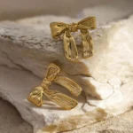 Photo de boucles d'oreilles dorées en forme de nœud, fabriquées en acier inoxydable, sur fond blanc.