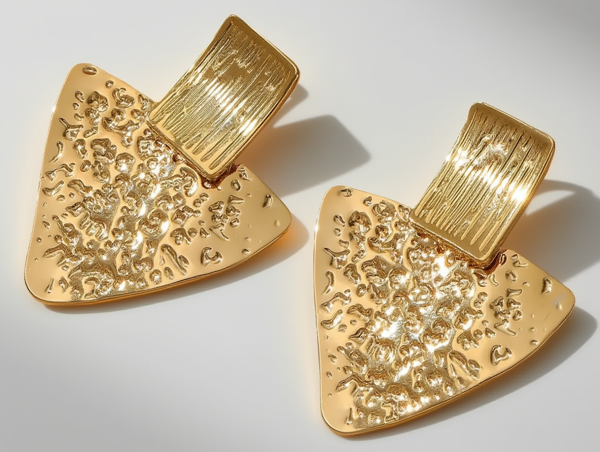 boucles-triangulaires-texturees-ACIER- INOYDABLEdorees.jpg Photo de boucles d'oreilles dorées en forme triangulaire avec une texture martelée, fabriquées en acier inoxydable, sur fond blanc.