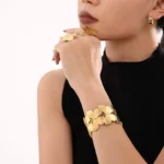 Photo d'un bracelet manchette doré avec un motif de papillons entrelacés, fabriqué en acier inoxydable, sur fond blanc.